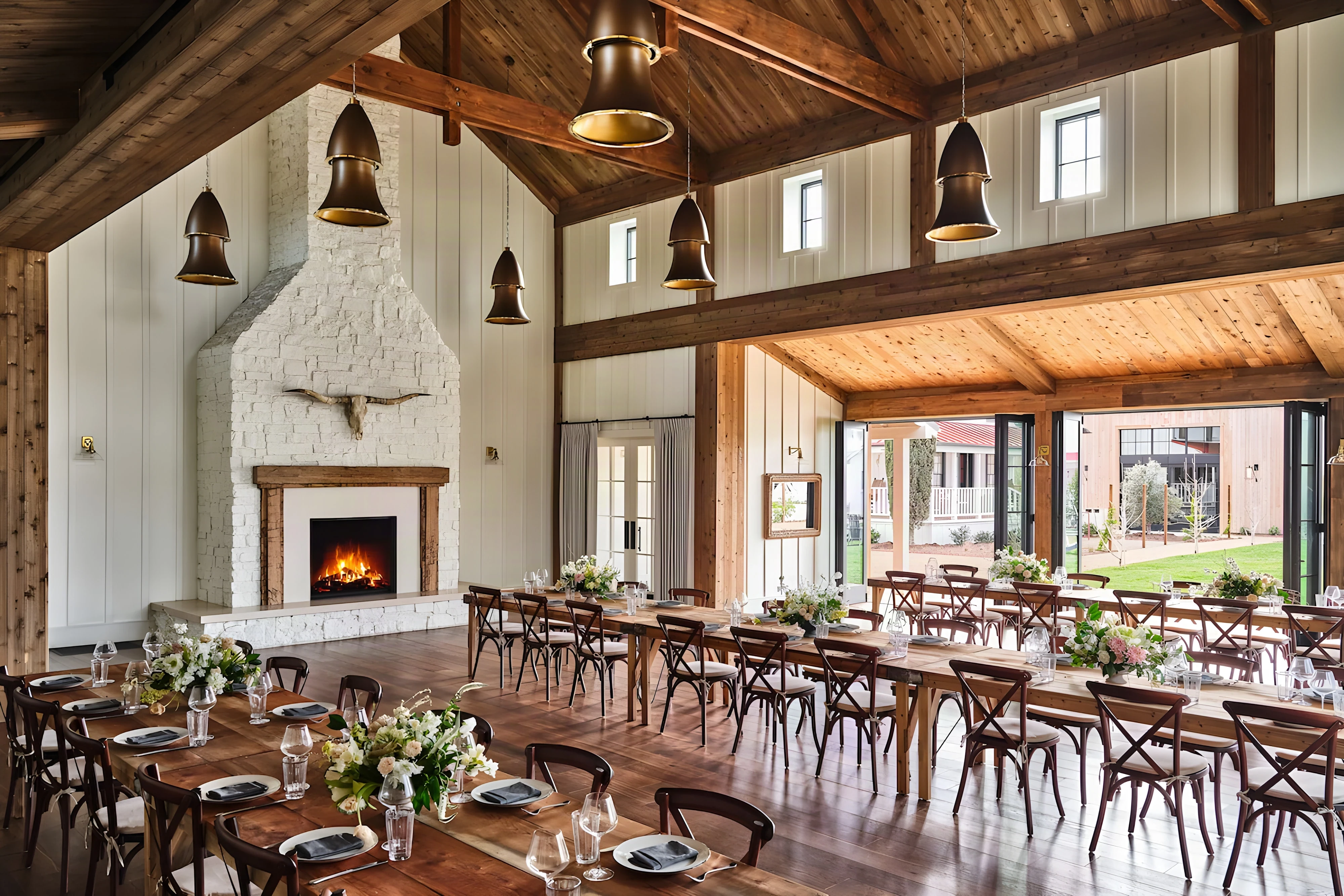 Barn at Mattei’s Inn set for dinner, with bell pendants, a lit stone fireplace and open garden doors