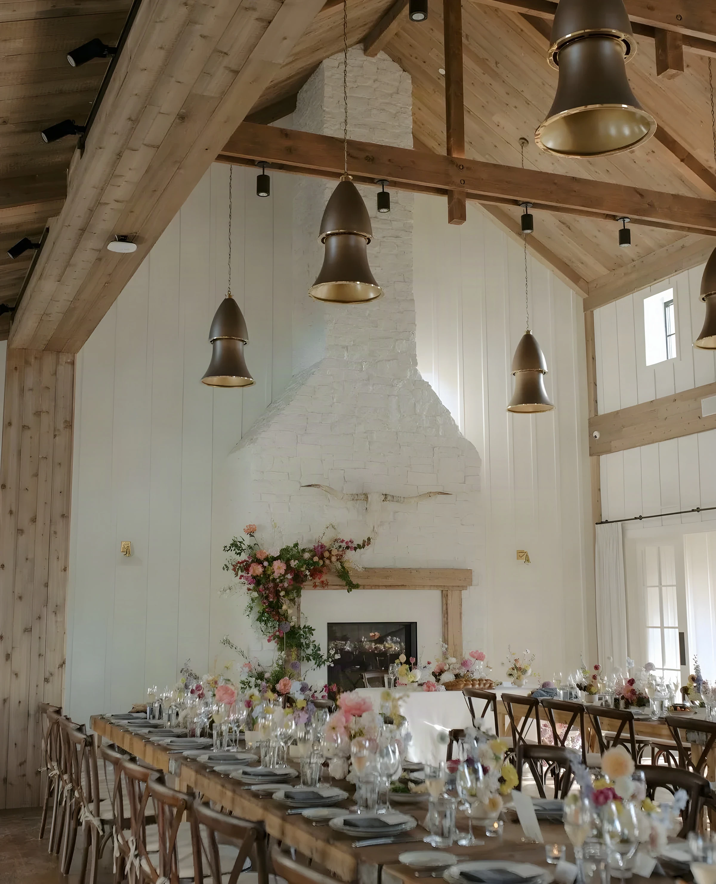Long dinner tables dressed with flowers before the stone fireplace in the Barn at Mattei’s Inn