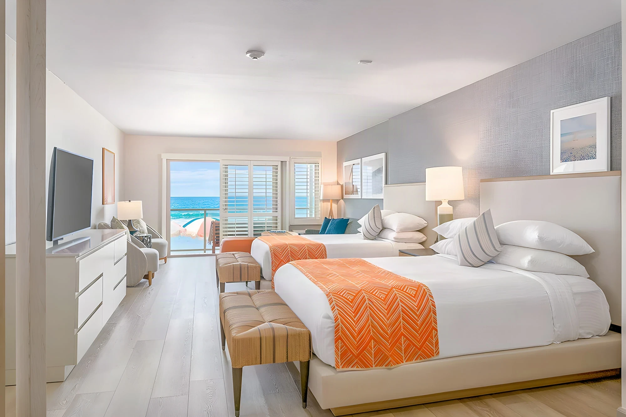 Double queen guest room with orange throws and a sliding door to an ocean balcony