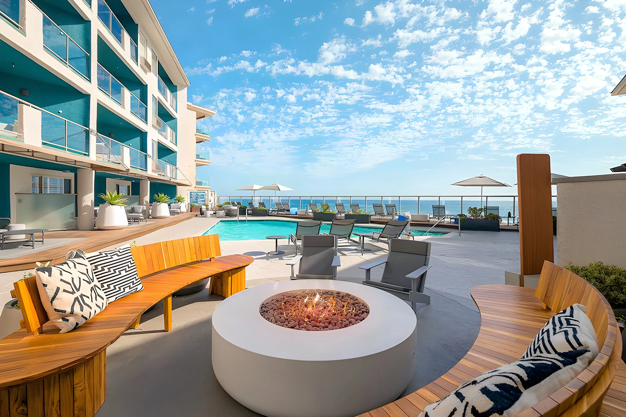 Beach Terrace Inn pool deck with a round fire pit, curved teak benches and the ocean beyond
