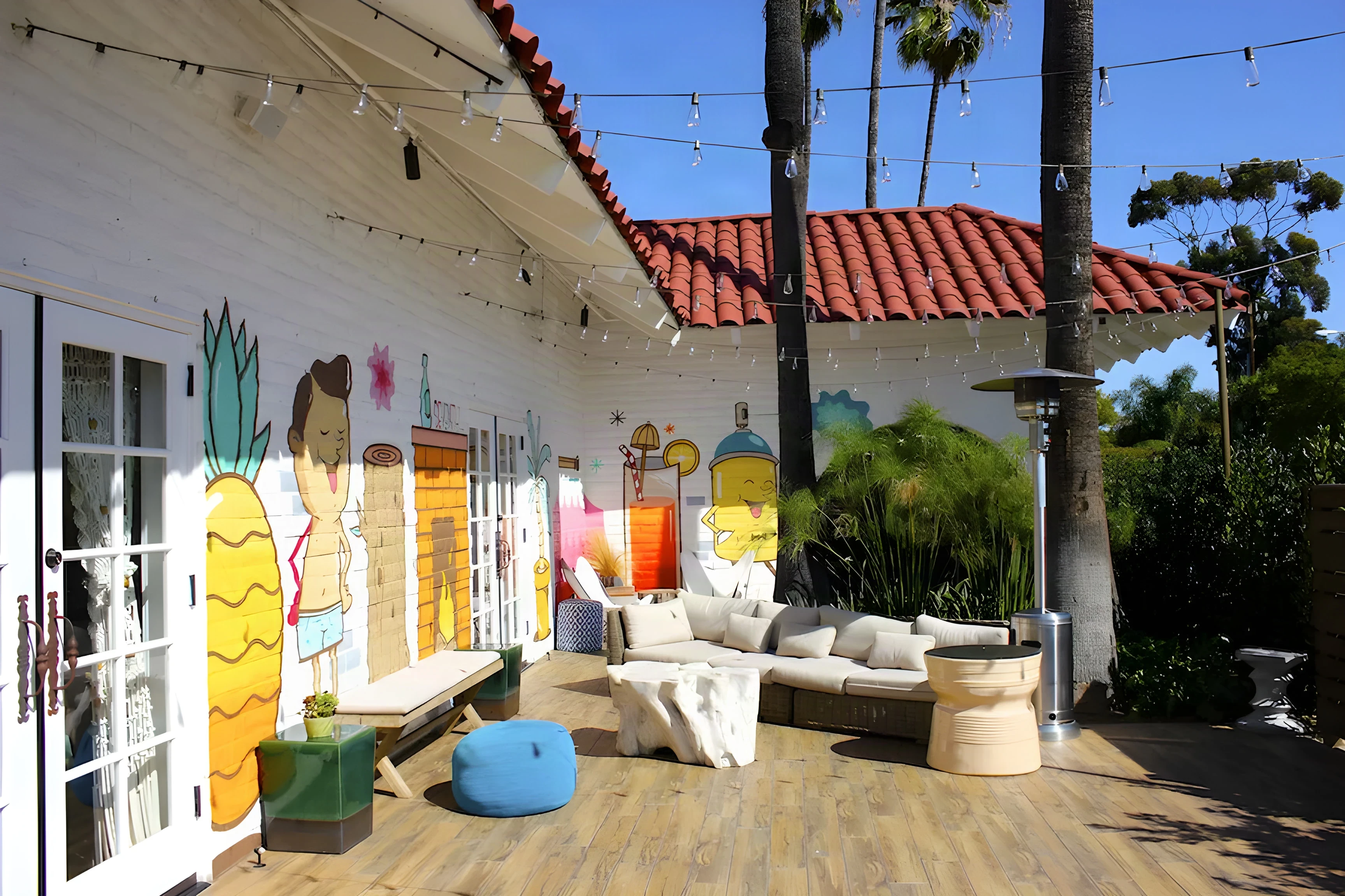 The Good Bar mural patio with white sofas, heaters and palms under string lights