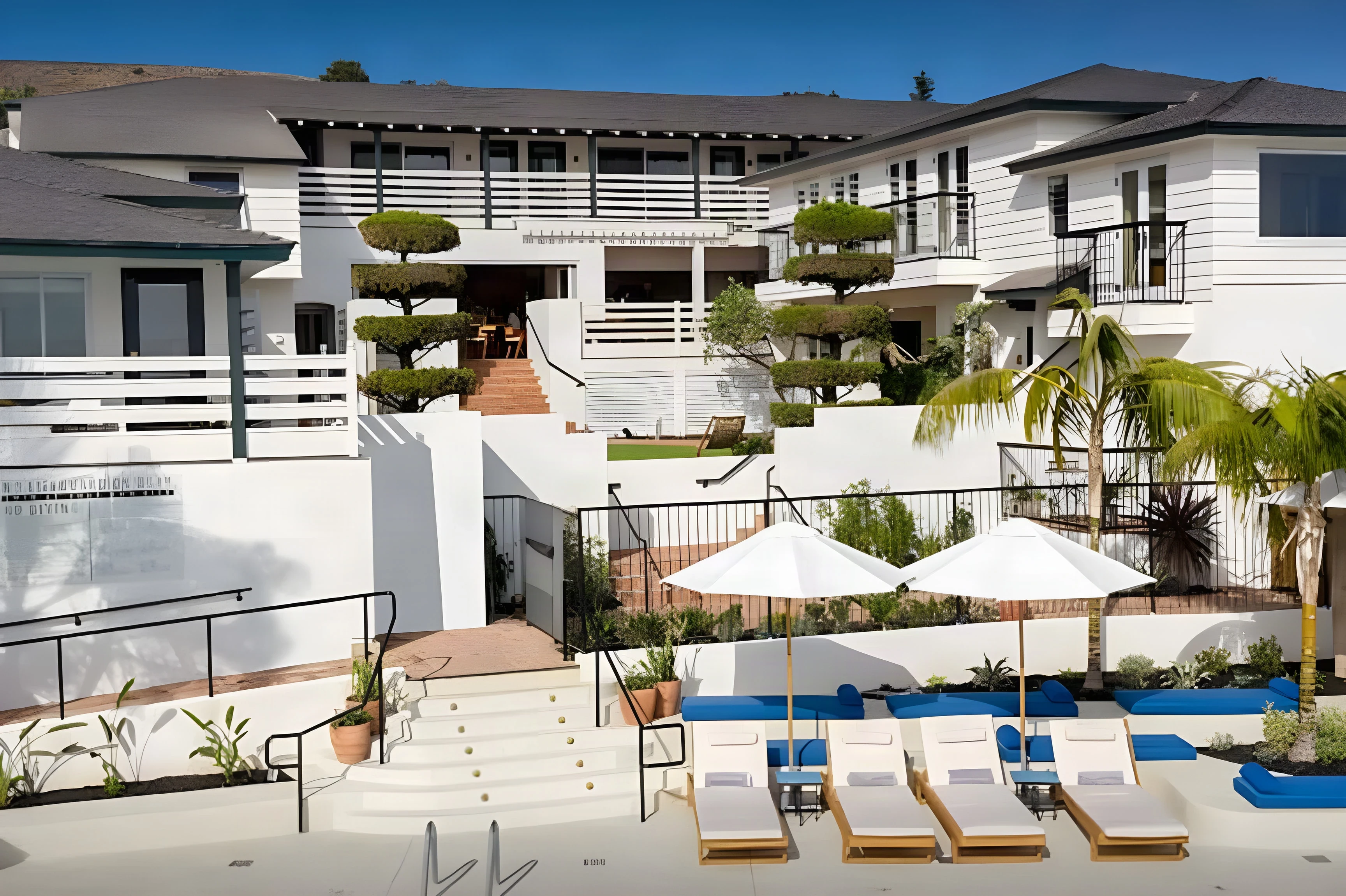 Renovated white Laguna Beach hotel rising above a pool terrace with blue umbrellas and loungers