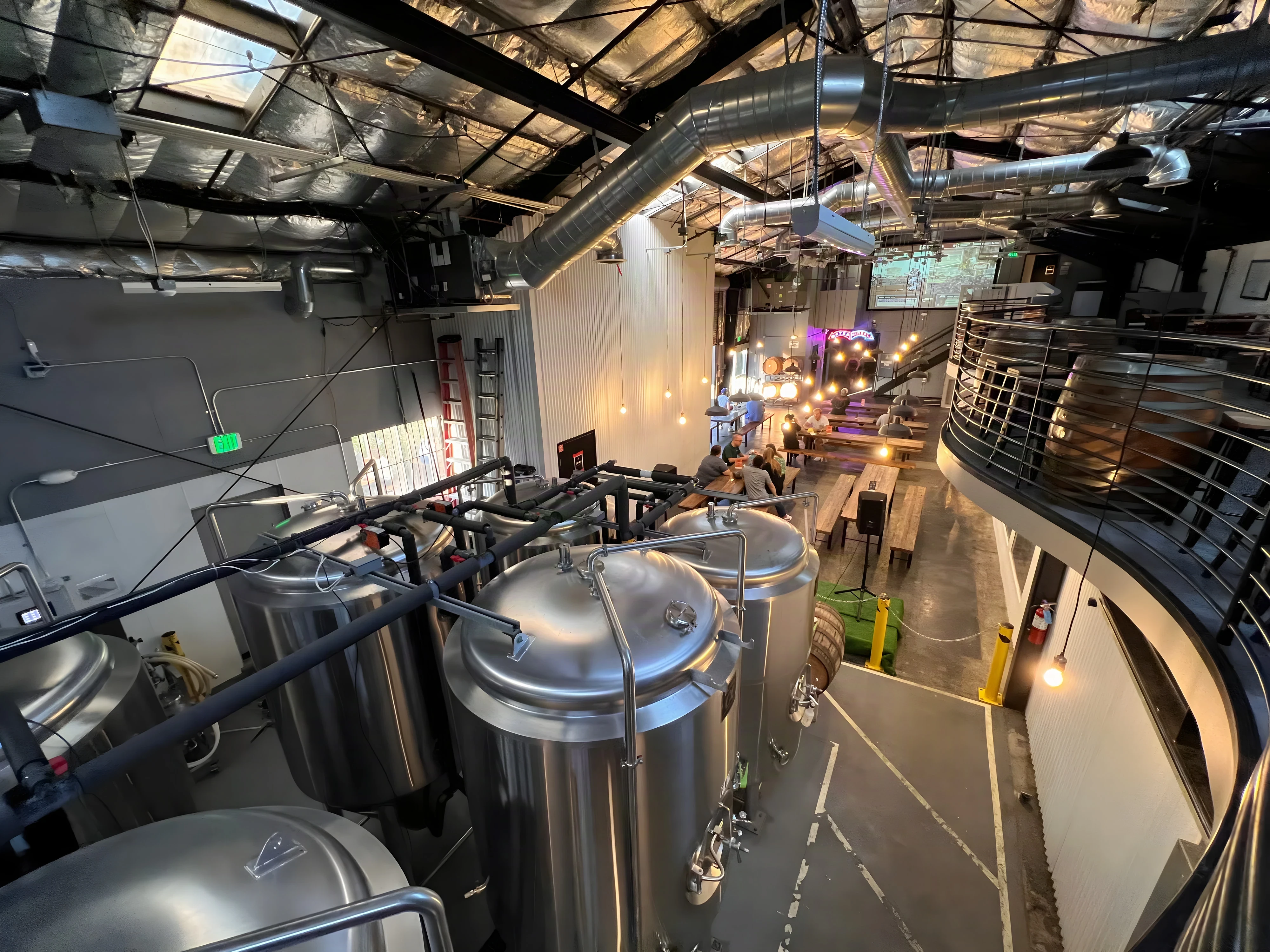 Stainless brewhouse tanks below the curved mezzanine railing inside Lawless Brewing Co.