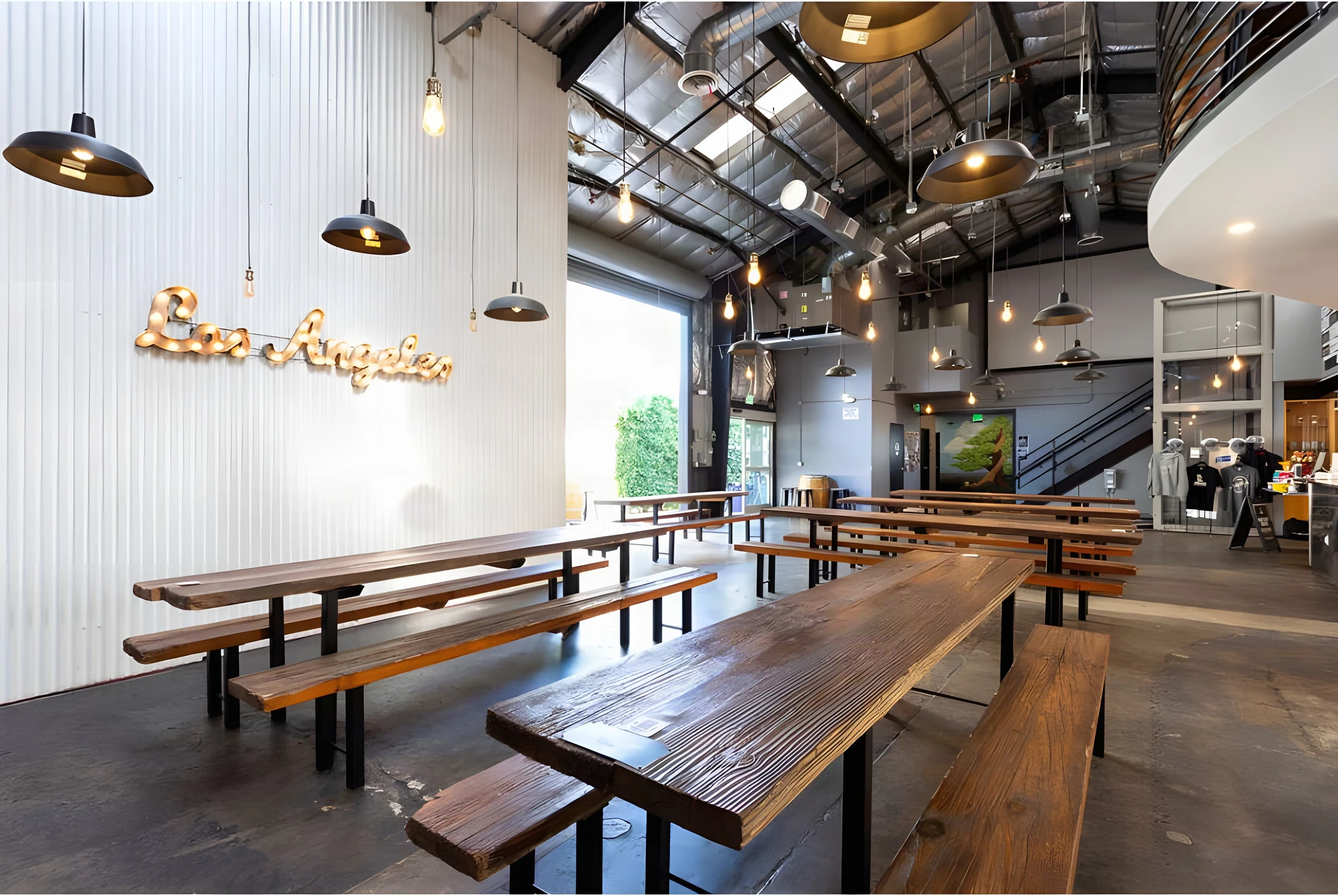 Communal timber tables under industrial pendants beside a lit Los Angeles sign at Lawless Brewing Co.