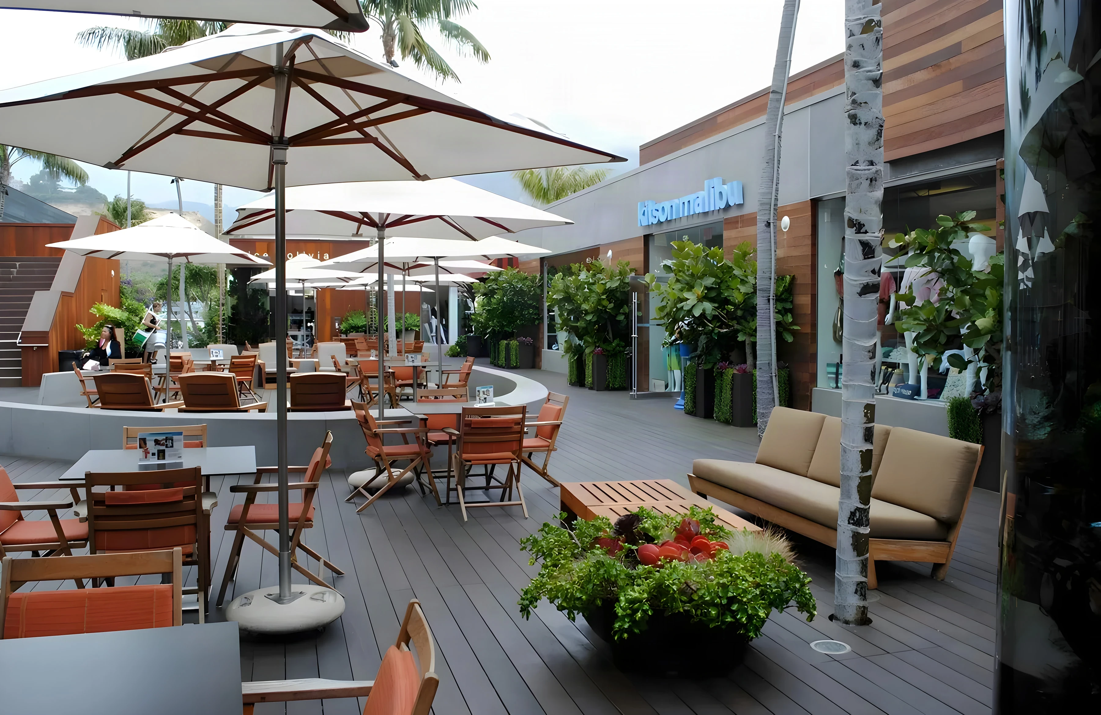 Malibu Lumber Yard café courtyard with white umbrellas, teak sofas and flower planters around the tables