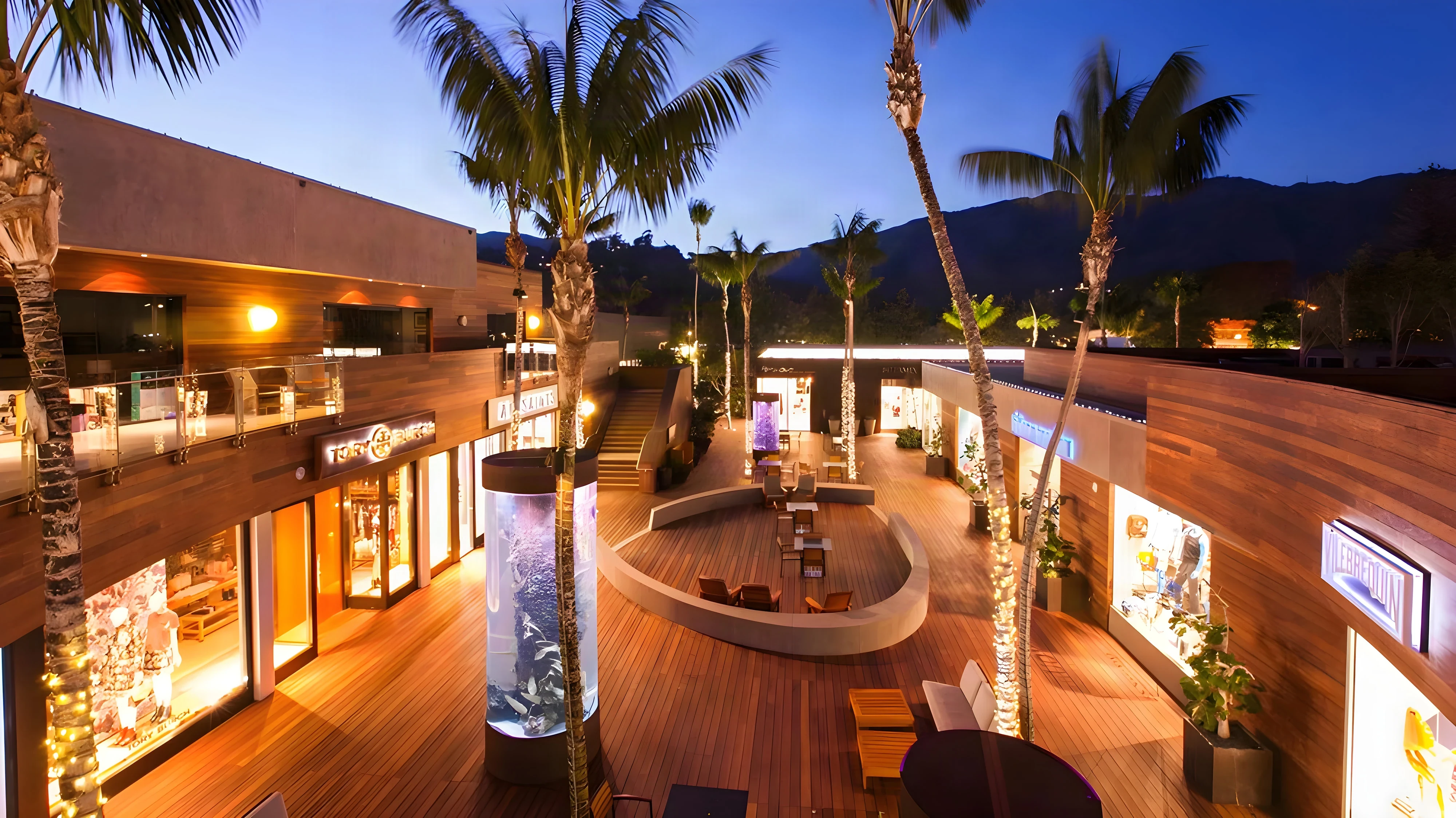 Malibu Lumber Yard plaza at dusk with lit louvered storefronts, palms and a timber deck