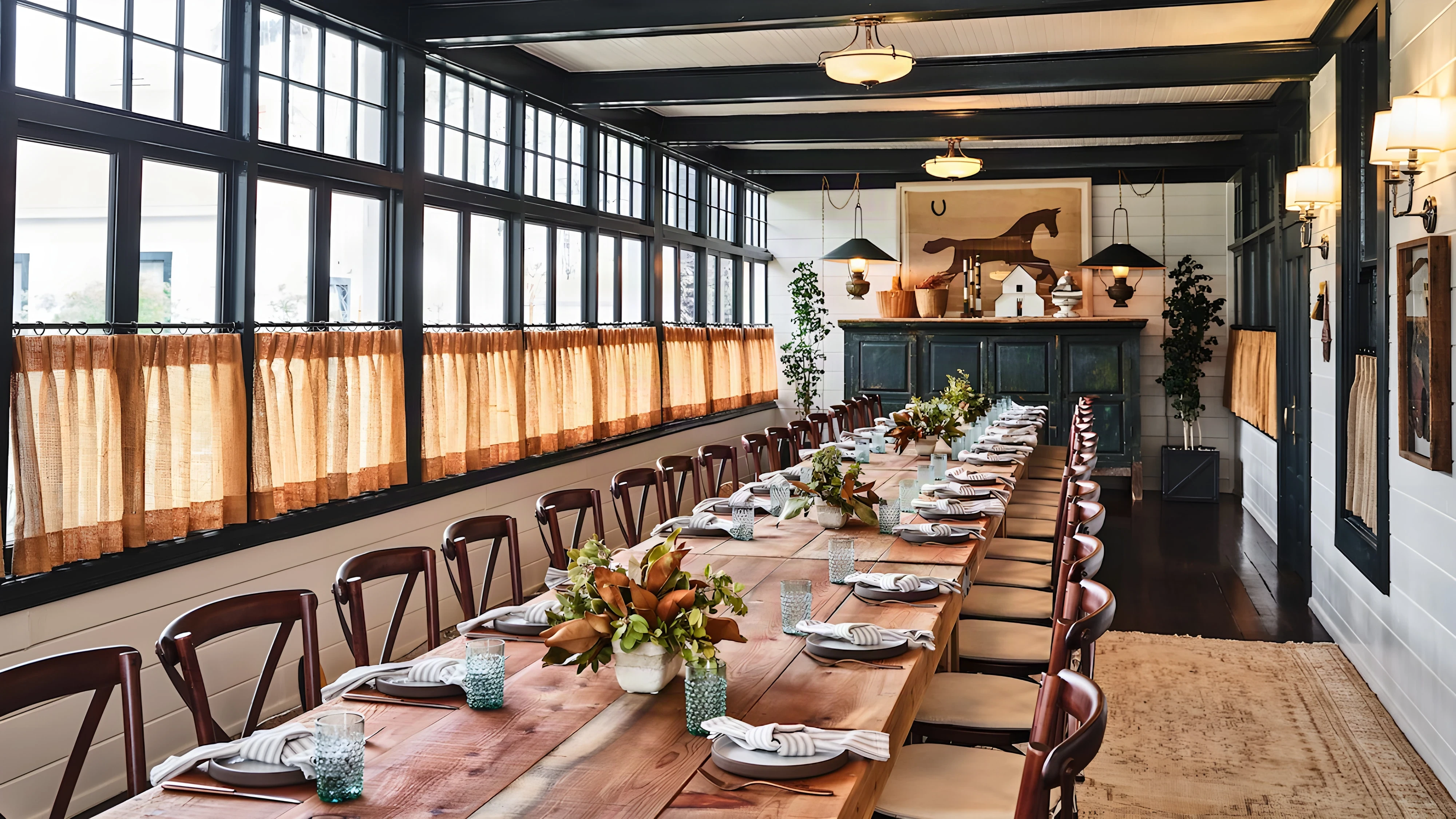 Long harvest table set for dinner under multi-pane windows and linen cafe curtains at Mattei’s Tavern
