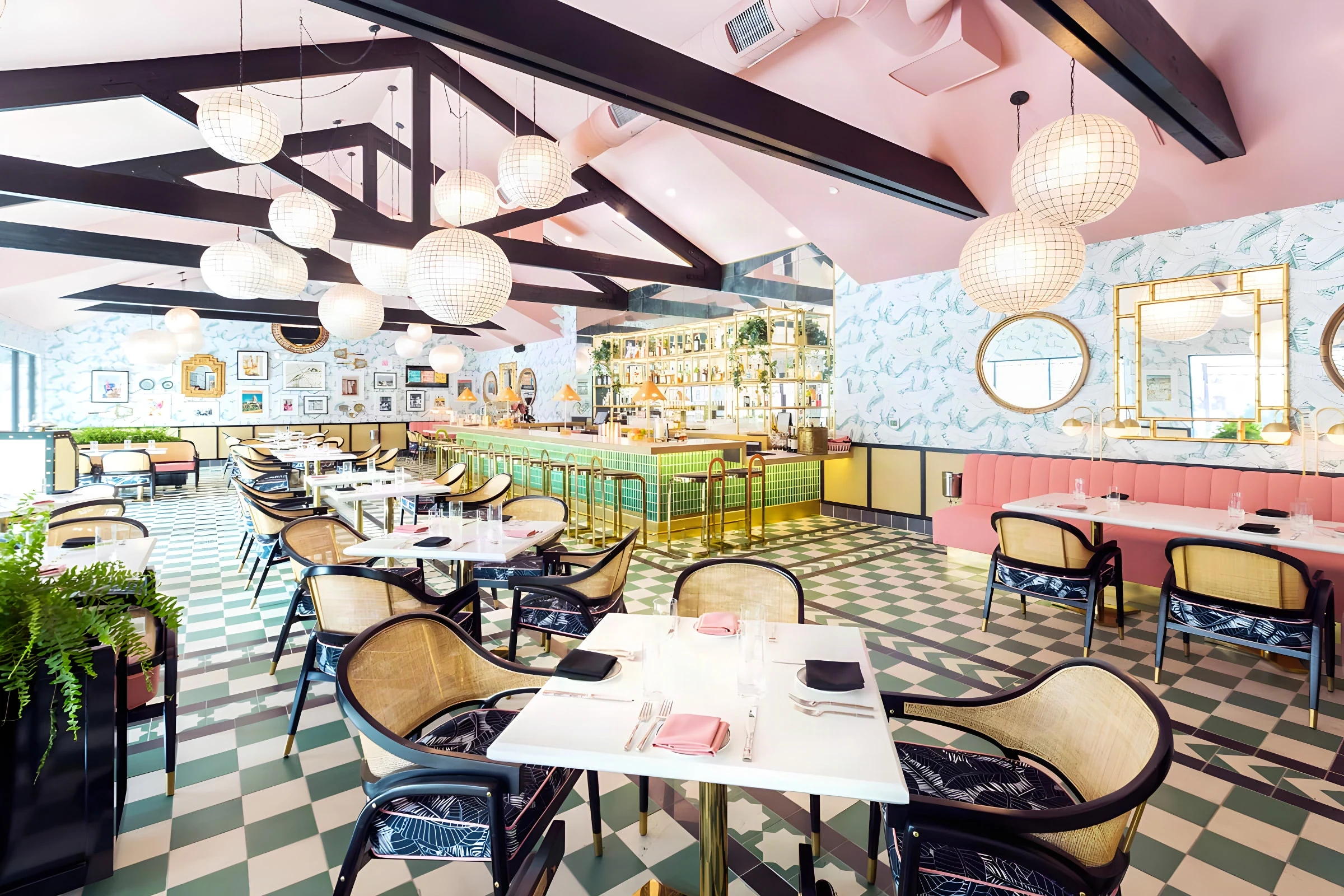 View across The Pink Cabana to the green tile bar under black beams and paper globe pendants