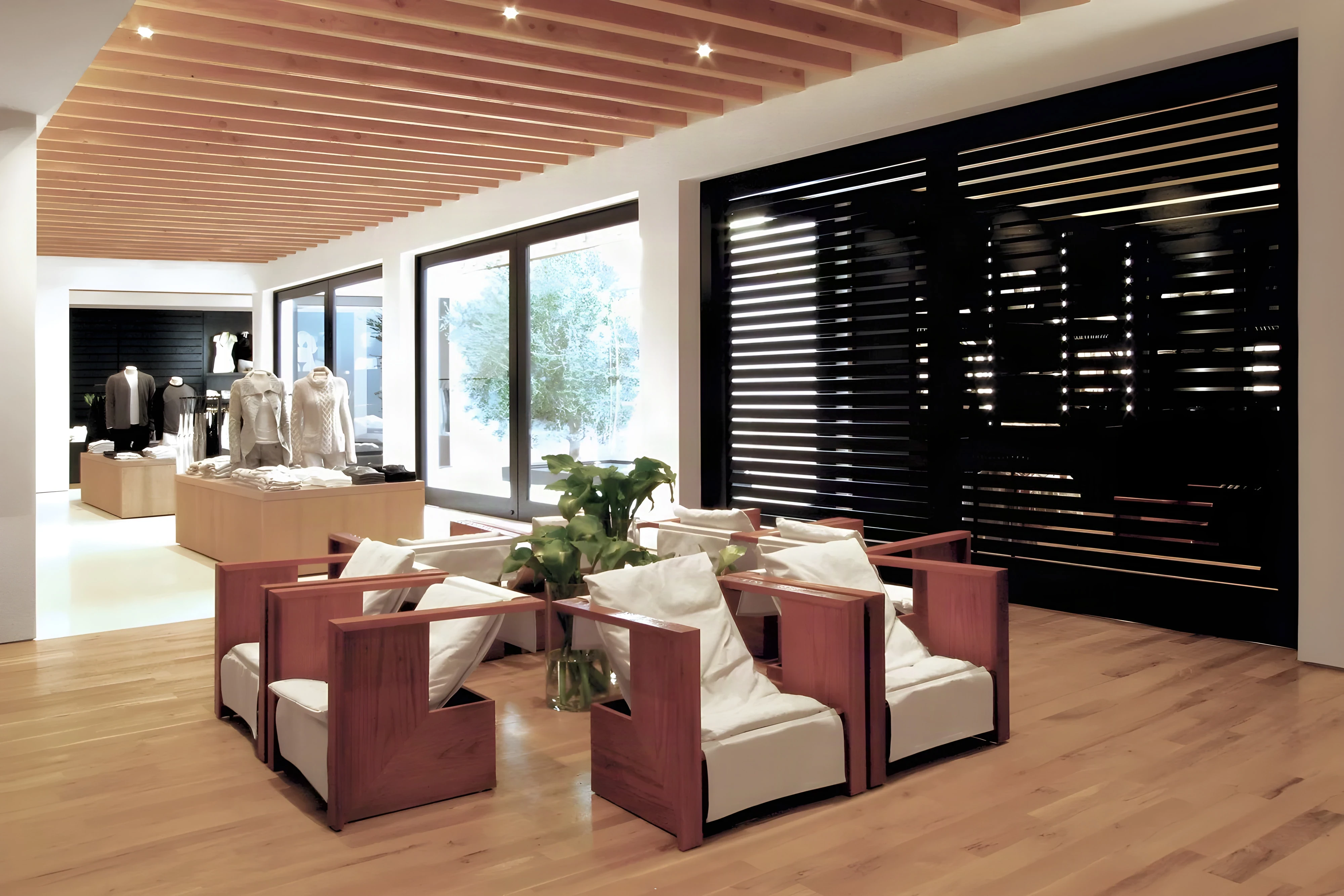 Store lounge with timber armchairs and white cushions beside black louvered screens