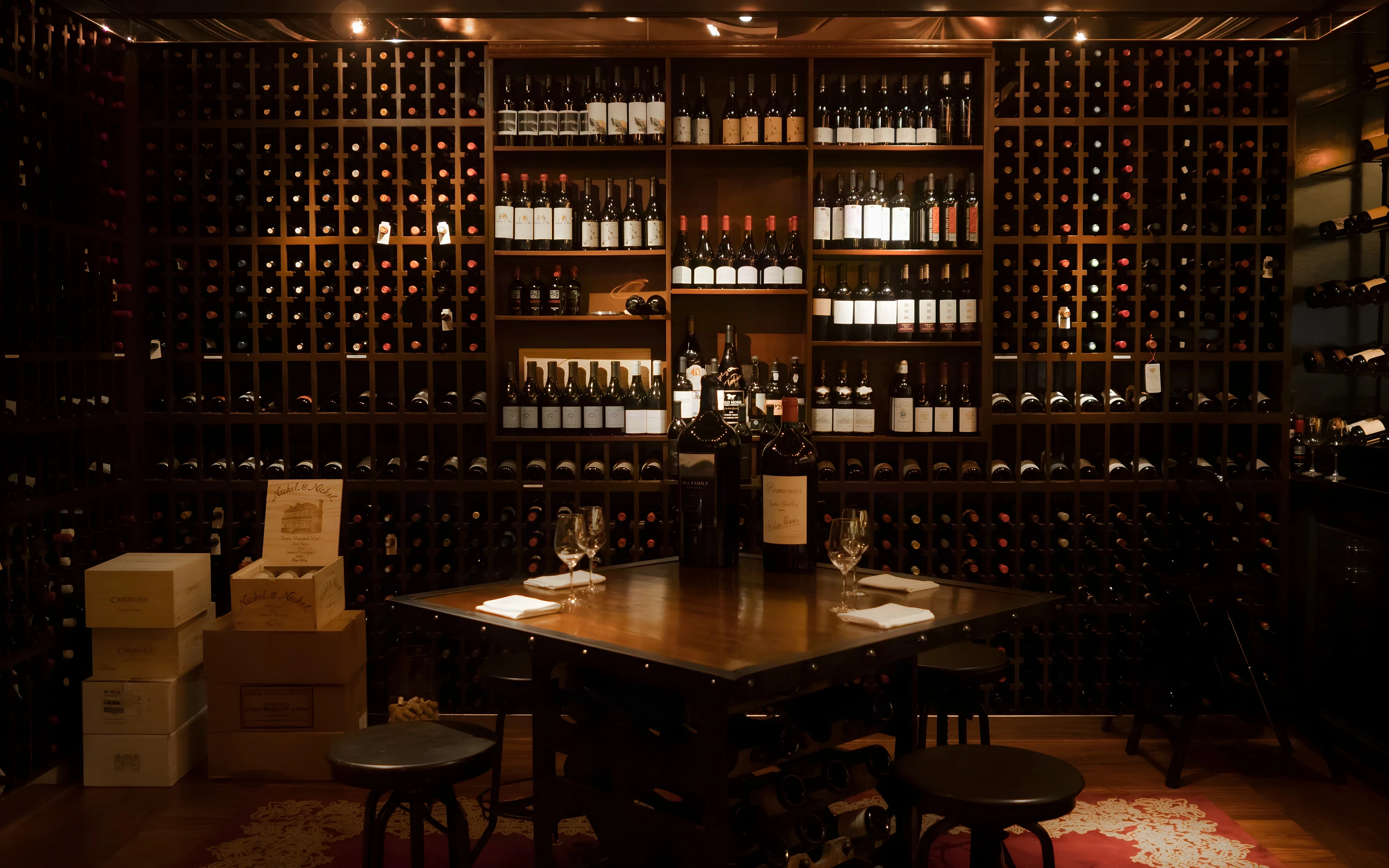 Tasting table and stools before floor-to-ceiling wine racks and cases inside the Royce Wine Room