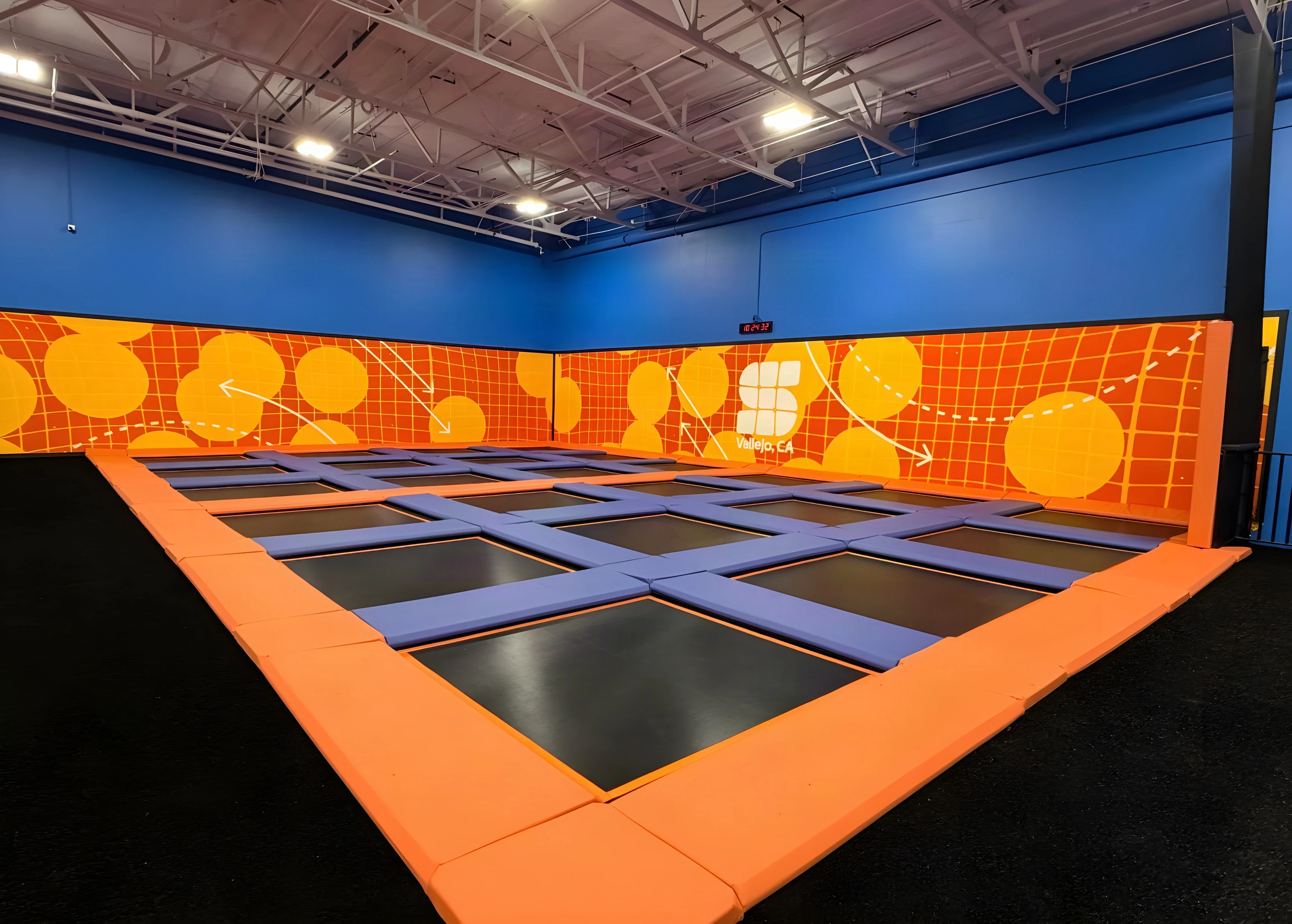 Orange-framed trampoline court beneath an orange mural wall at Sky Zone Frisco