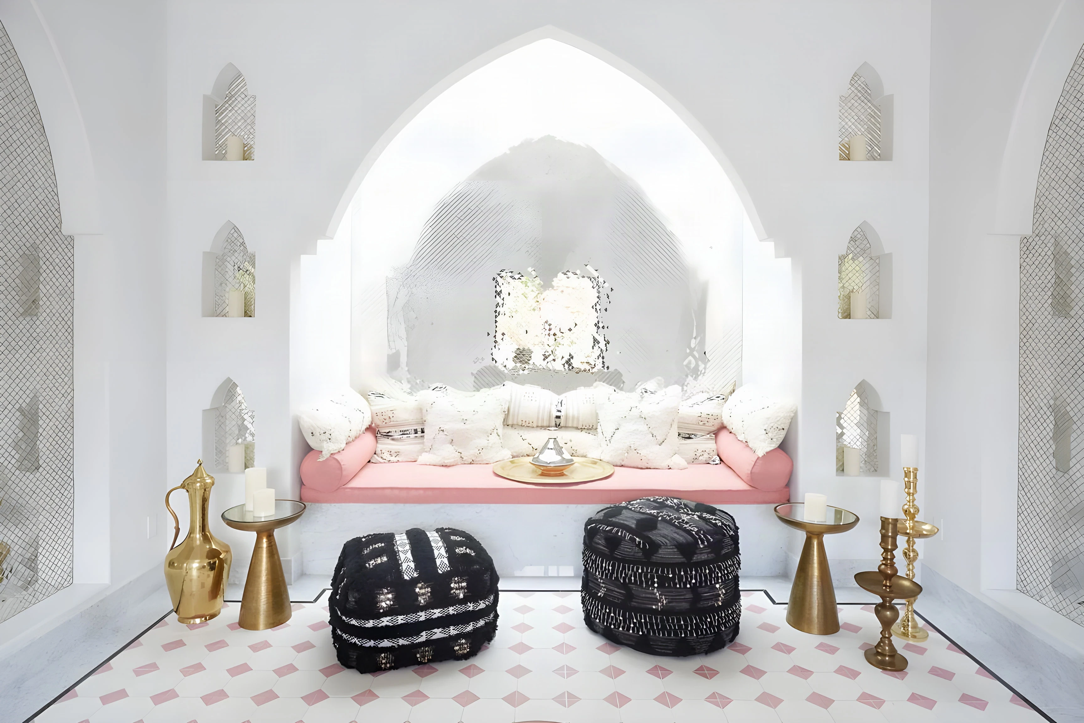 Pointed white arch over a pink daybed with black poufs and brass tables inside The Spa at Indian Wells