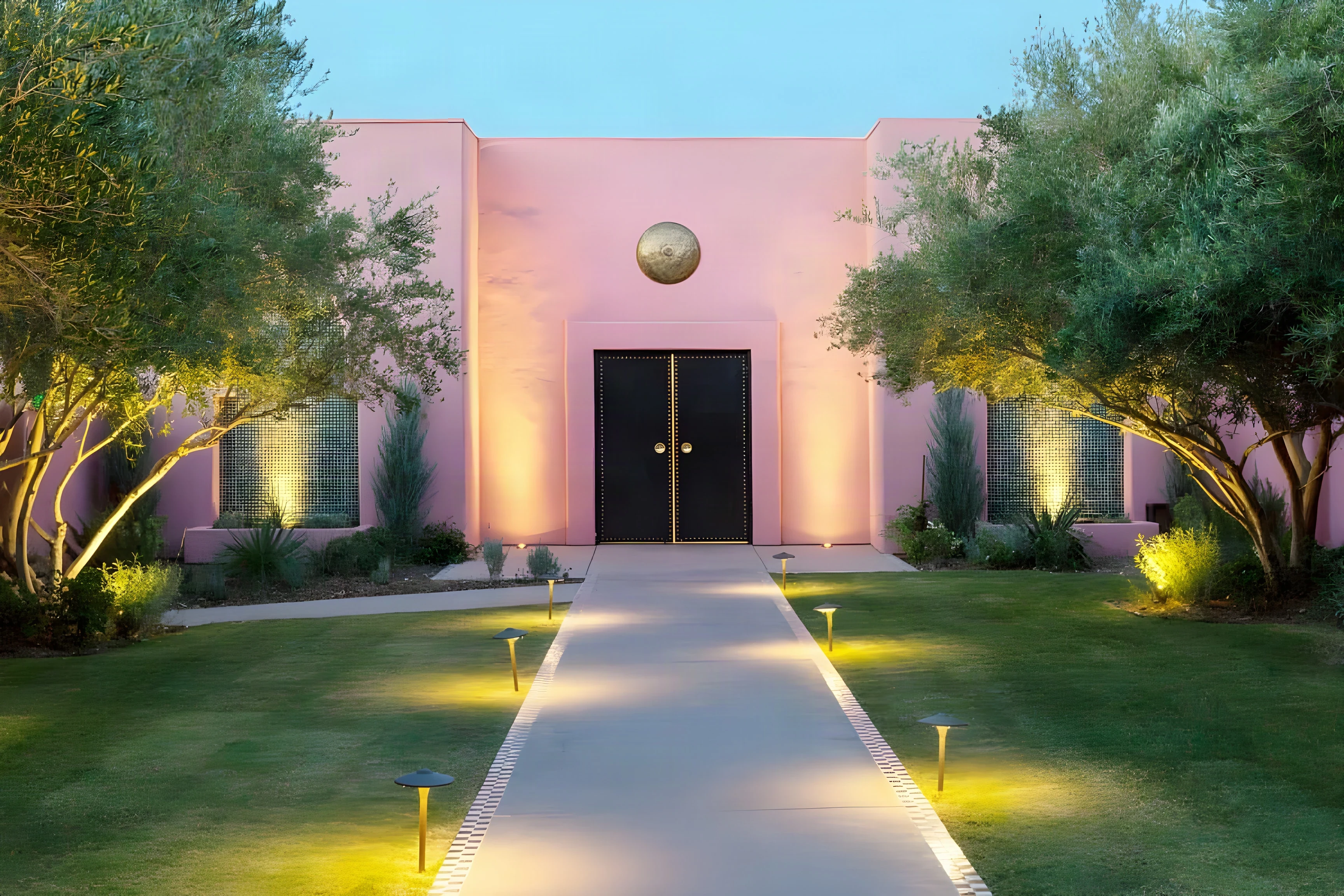 Pink stucco spa entrance at dusk with a lit garden path and olive trees in Indian Wells