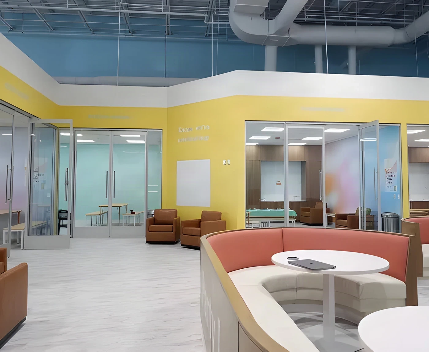 Bright yellow lounge with curved coral booth and glass party rooms at Cloudbound kids play park